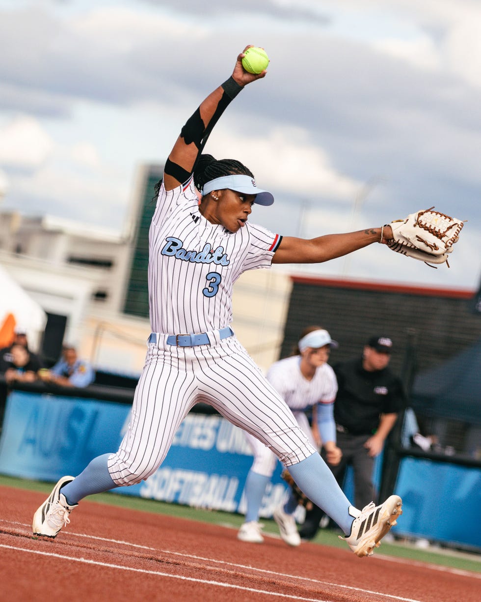 Softball player in a striped uniform pitching with a raised arm and ball, focused on the game. Softball player in a striped uniform pitching with a raised arm and ball, focused on the game.