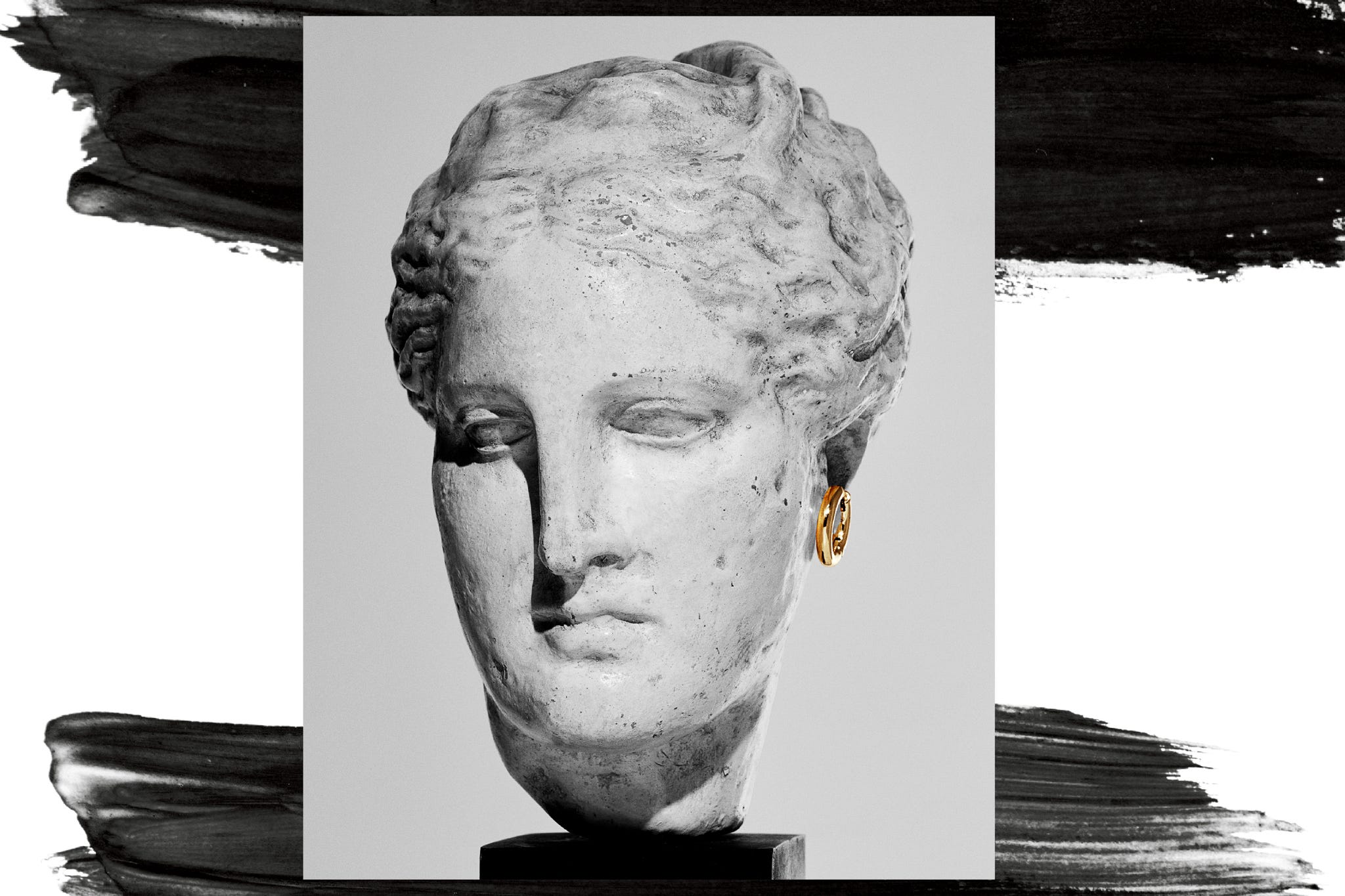 Head of a classical statue adorned with a gold earring, displayed against a contrasting background. Head of a classical statue adorned with a gold earring, displayed against a contrasting background.