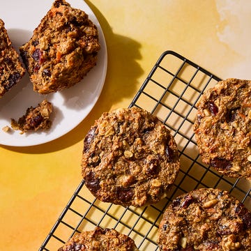 Baked oatmeal cookies on a cooling rack with a slice on a plate and a yellow background.