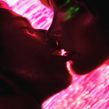 Young couple about to kiss, fibre optics in background, close-up Intimate moment between two people kissing, set against a vibrant pink background.