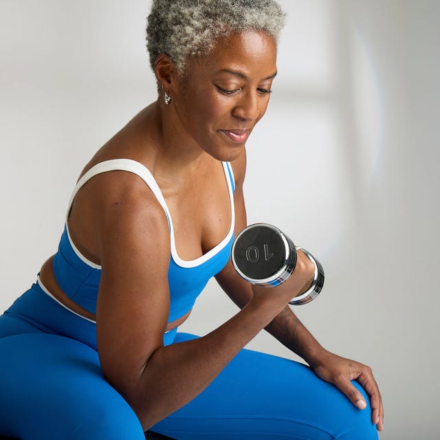 A woman with short gray hair exercises with a dumbbell, wearing a blue workout outfit, focusing on her strength training.