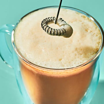 Close-up of a frothy beverage in a clear glass, with a metallic stirrer resting on the foam.