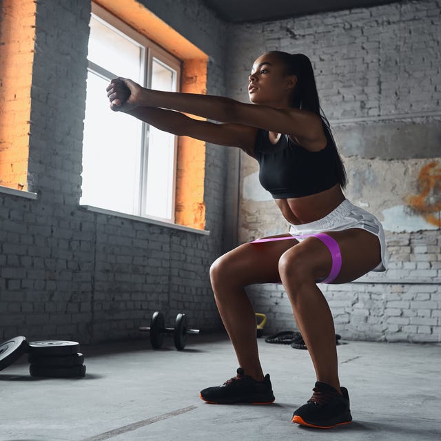 Full length of young African woman using elastic resistance band while exercising in gym