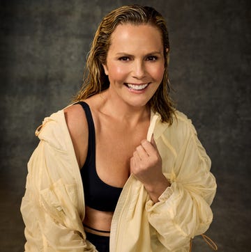 person smiling in a yellow jacket and black sportswear against a dark background.