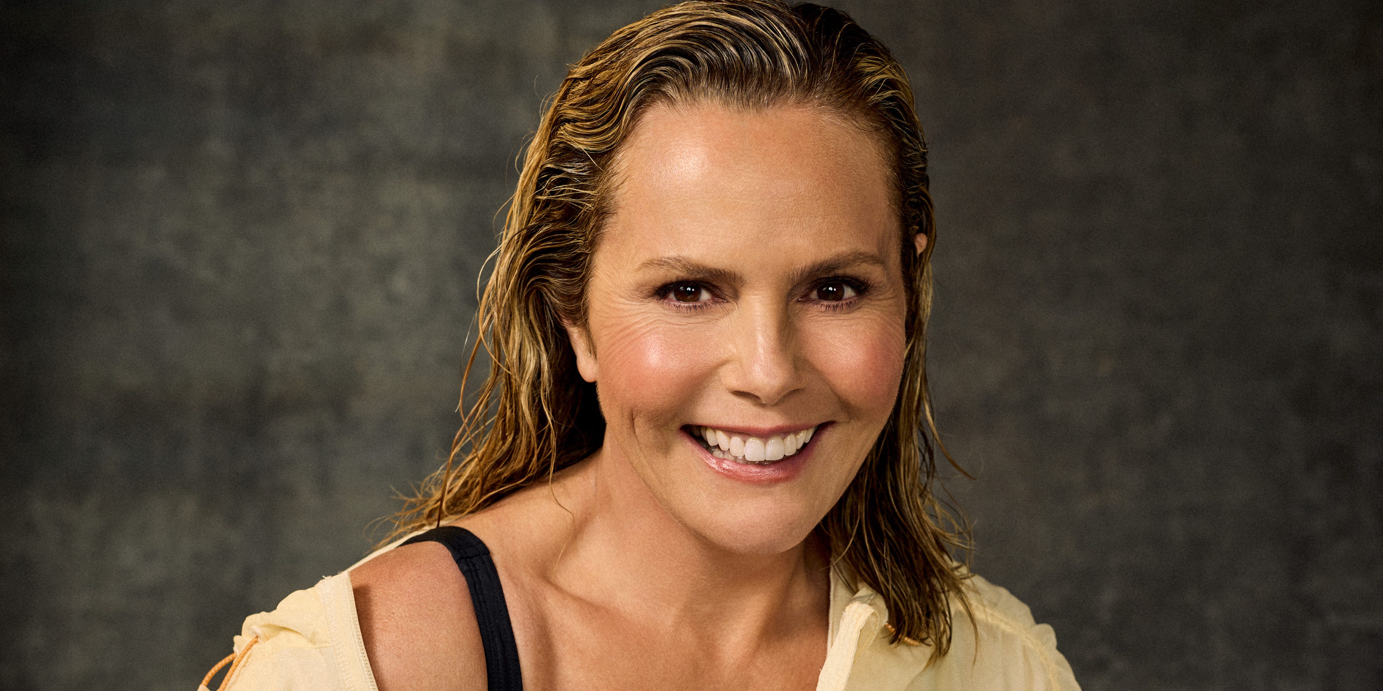 person smiling in a yellow jacket and black sportswear against a dark background.