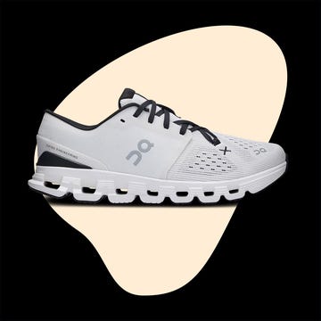White running shoes with black laces displayed from the side and worn on feet, showing a sandy ground beneath. White running shoes with black laces displayed from the side and worn on feet, showing a sandy ground beneath.