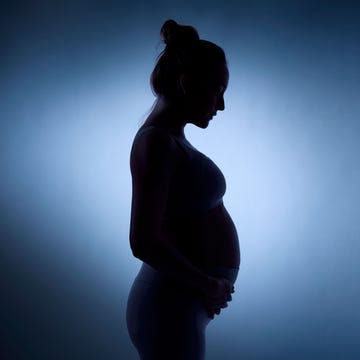 Silhouette of a pregnant woman holding her belly against a softly lit background. Silhouette of a pregnant woman holding her belly against a softly lit background.