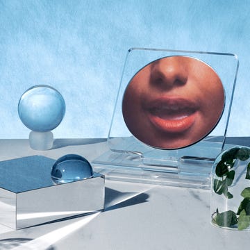 A stylized arrangement of objects including a reflective surface a clear faceshaped panel and a glass with shadows on a marble surface