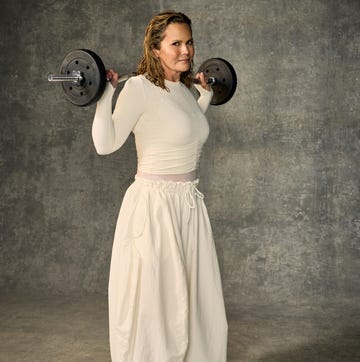 person in white outfit lifting a barbell on shoulders against textured background.