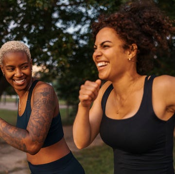 Two women jogging and laughing outdoors in athletic wear.