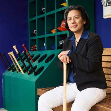 Person seated with a baseball bat and colorful caps in the background.