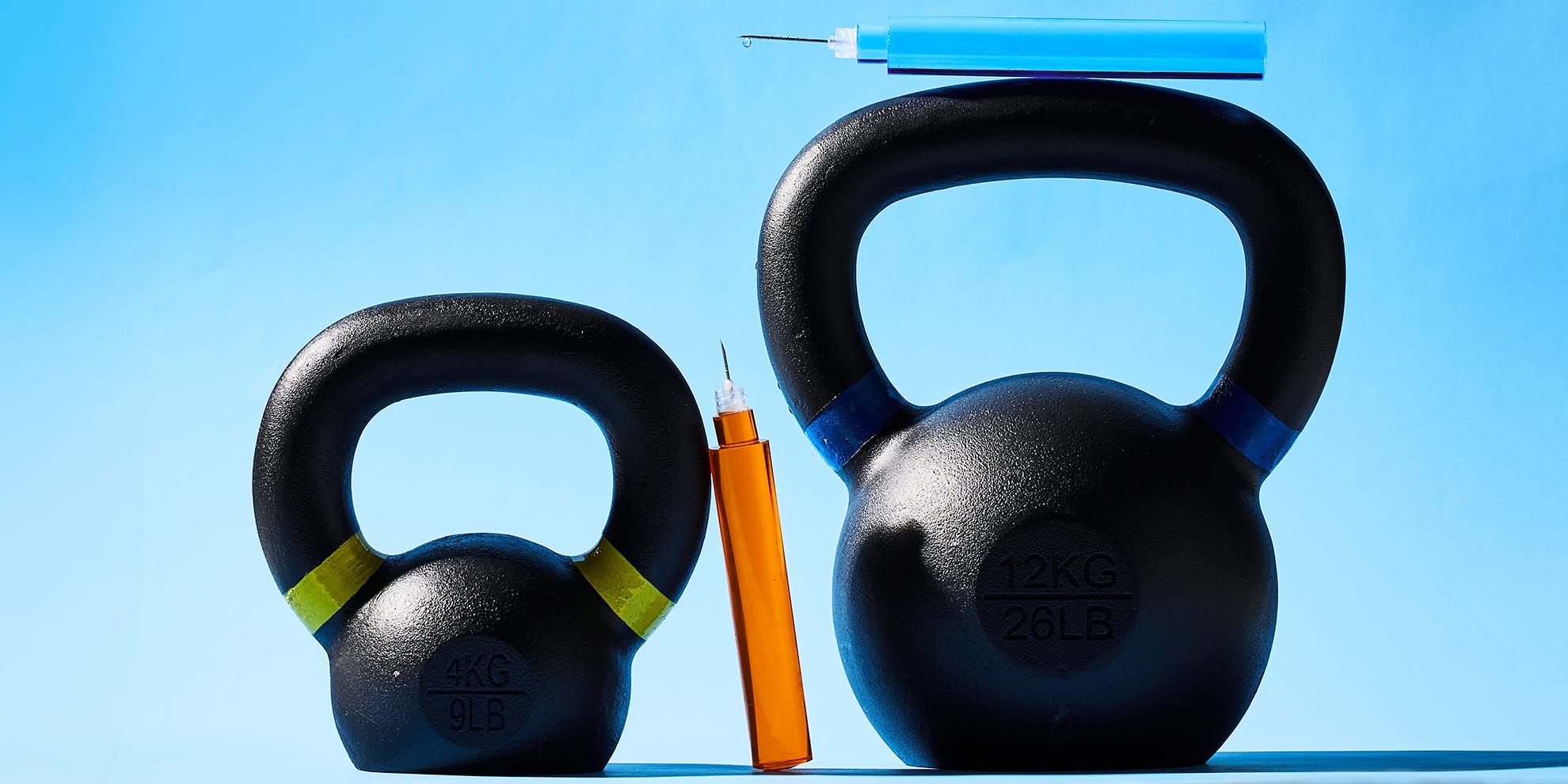 Two kettlebells in black with colored markings and syringes above them, set against a light blue background.