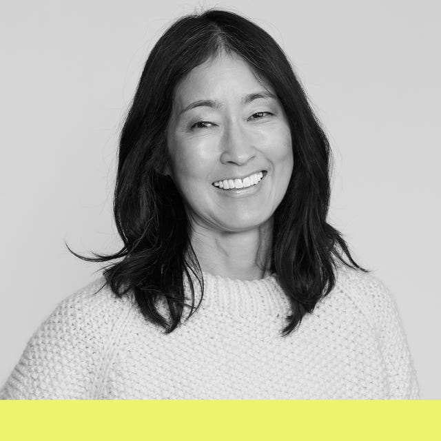 Smiling woman with long dark hair wearing a white sweater, set against a light background with a yellow accent at the bottom.