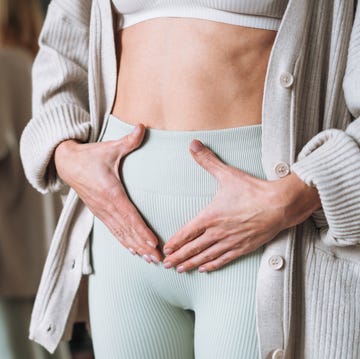 woman holding lower abdomen at home, portraying bloating discomfort
