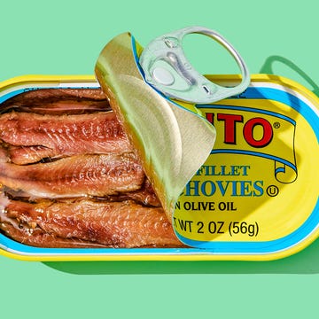 Open tin of anchovies in olive oil on a green background.