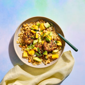 Bowl of quinoa topped with grilled patties, mango, avocado, green onions, and cashews, served with a fork and napkin.