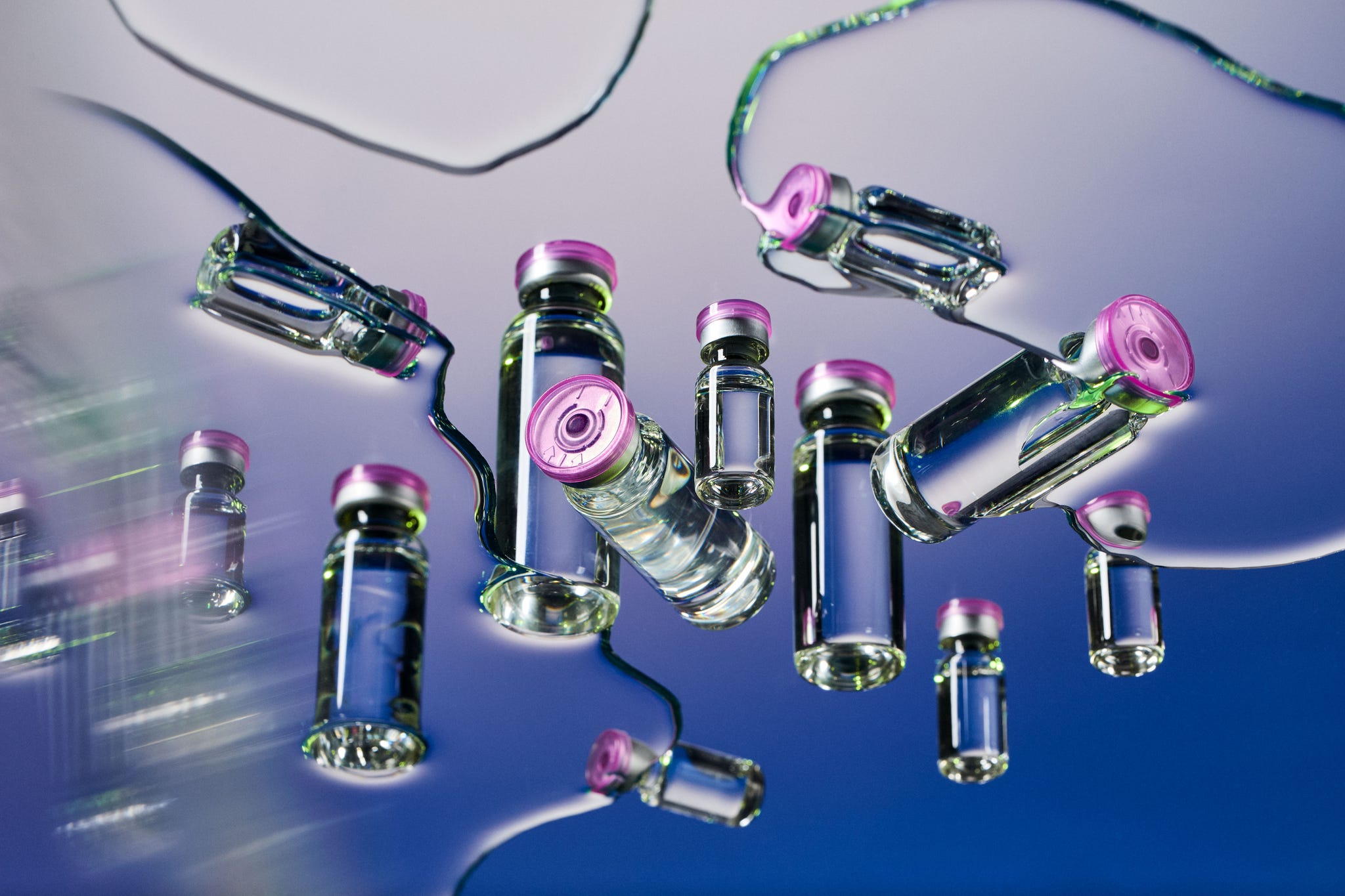 Floating glass vials with pink caps against a reflective and colorful background. Floating glass vials with pink caps against a reflective and colorful background.