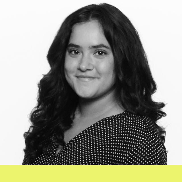 Smiling young woman with curly hair, wearing a polka dot top against a white background with a yellow bottom bar.