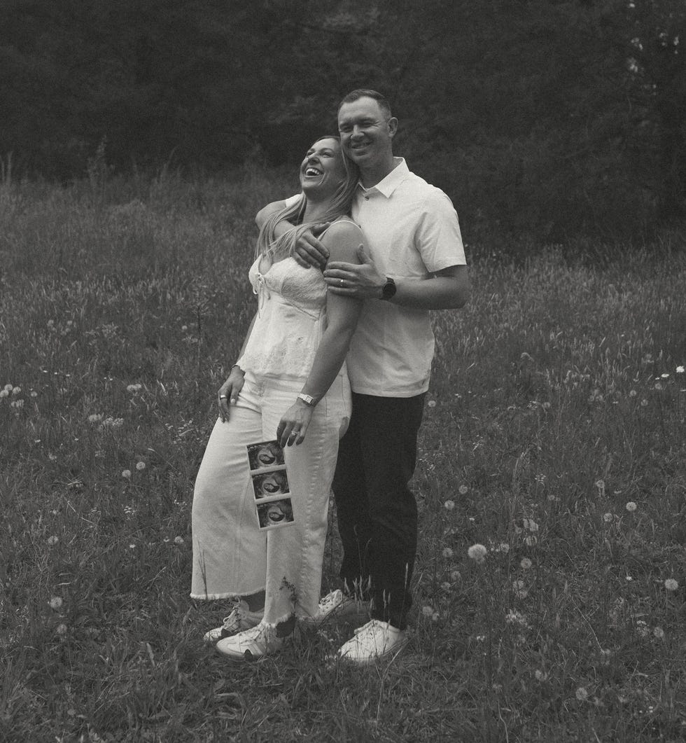 Couple laughing and embracing outdoors while holding ultrasound photos in a grassy field. Couple laughing and embracing outdoors while holding ultrasound photos in a grassy field.