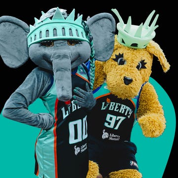 Two mascots dressed as the Statue of Liberty, posing together in colorful sports jerseys against a bold background.