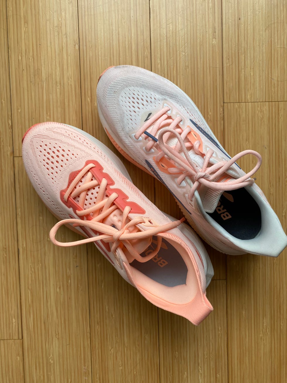 Pair of athletic shoes with light colors and contrasting laces set on a wooden surface. Pair of athletic shoes with light colors and contrasting laces set on a wooden surface.