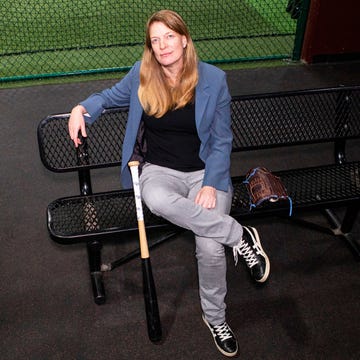 Individual seated on a bench in a sports facility with a bat.