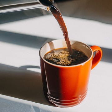 pouring coffee into an orange mug on a sunny table