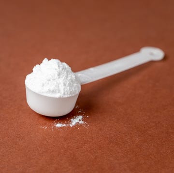 measuring scoop with creatine powder on brown background, sports nutrition and supplement