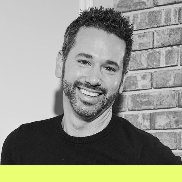 man wearing a dark sweater in front of a brick wall with a bright yellow bottom