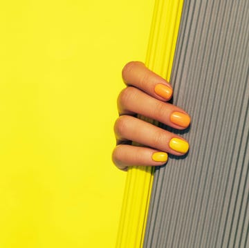 hand with colorful nails holding a textured gray surface against a bright yellow background