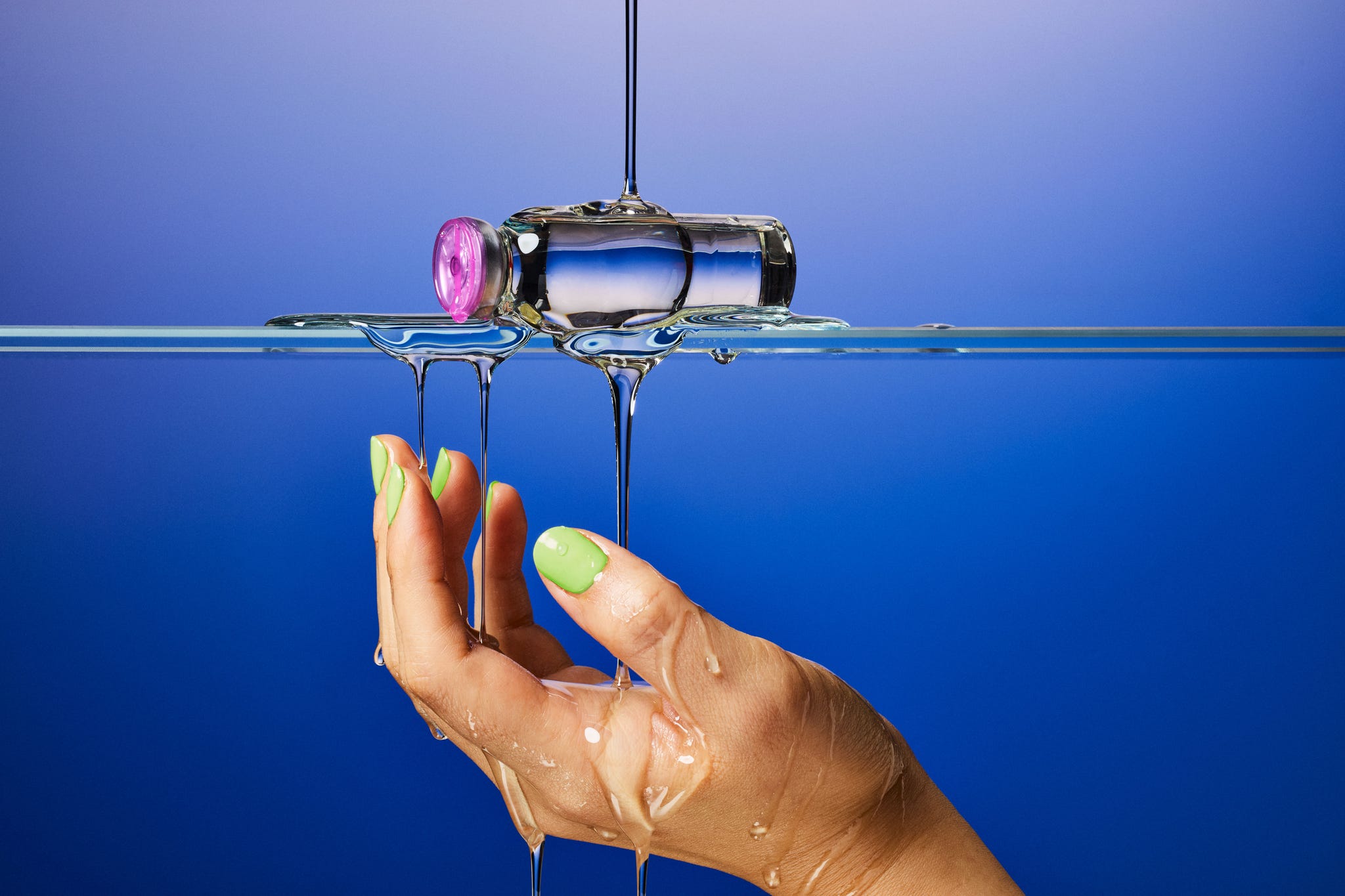 A hand holding a glass bottle dripping with liquid against a blue background. A hand holding a glass bottle dripping with liquid against a blue background.