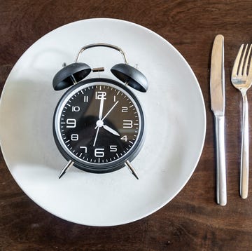 Intermittent fasting, trend 16:8 fasten, alarm clock on plate Alarm clock on a plate with knife and fork on wooden table