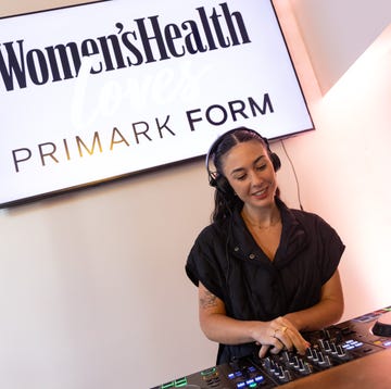 DJ performing at an event featuring a Women's Health and Primark collaboration sign in the background.