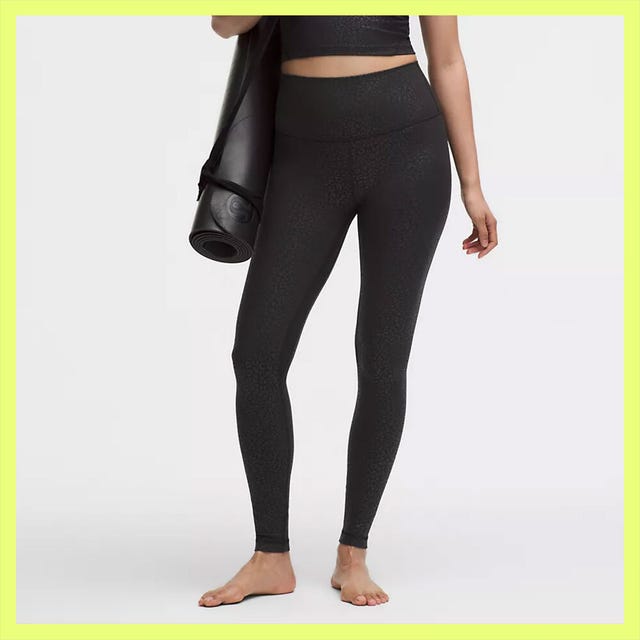 Black leggings and bright pink athletic shoes with a yoga mat in the background.
