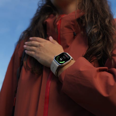 person wearing an orange jacket checking a smartwatch with outdoor activity display.