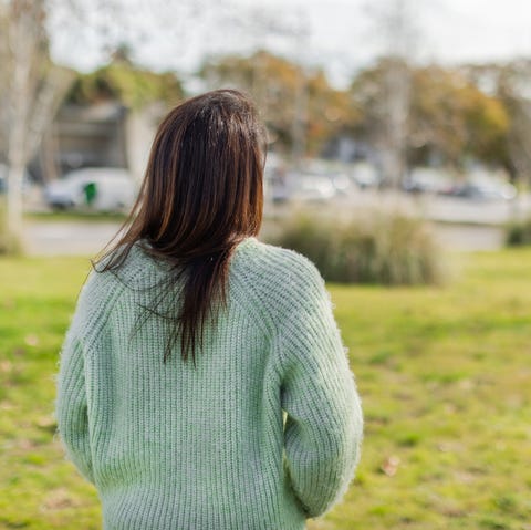 unrecognizable woman wearing a green sweater stands in a city park, looking at nature and the urban landscape. tranquil and reflective moment. horizontal composition with copy space.
