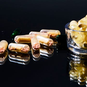Clear capsules with powder inside on a black reflective surface, beside a glass bowl.