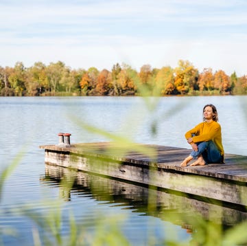 person sitting on a dock over a calm lake surrounded by autumn trees.
