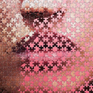 Close-up of a partially completed jigsaw puzzle featuring a stylized depiction of lips and facial features. Close-up of a partially completed jigsaw puzzle featuring a stylized depiction of lips and facial features.