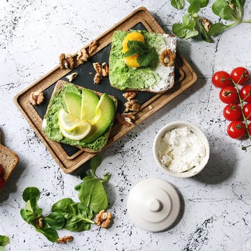 vegetarian sandwiches with avocado, ricotta, egg yolk, spinach, cherry tomatoes on whole grain toast bread on wooden slate board with ingredients above over white marble background top view, space. (photo by: natasha breen/reda/universal images group via getty images)