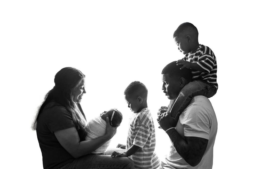 A family with two children and a newborn, sitting and interacting together in a bright, high-contrast setting. A family with two children and a newborn, sitting and interacting together in a bright, high-contrast setting.