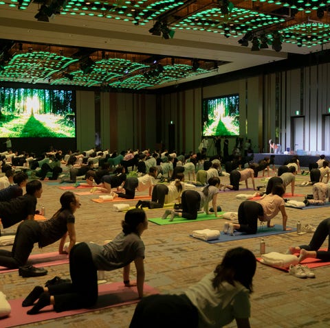 people doing yoga on mats in a large conference room with screens displaying nature scenes.