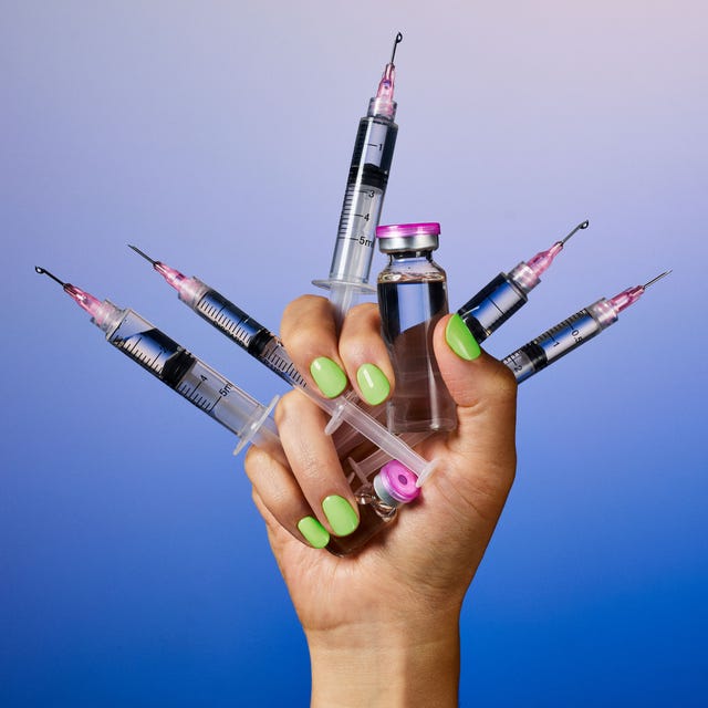 A hand holding multiple syringes and a vial against a gradient blue background.