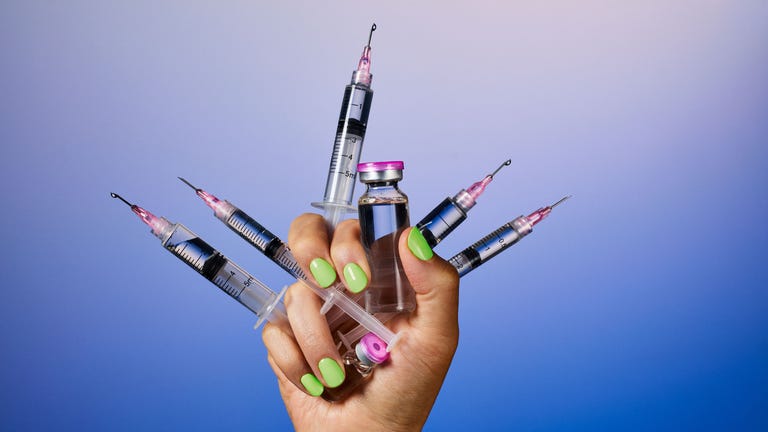 A hand holding multiple syringes and a vial against a gradient blue background. A hand holding multiple syringes and a vial against a gradient blue background.