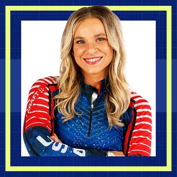 Smiling athlete wearing a blue and red sports outfit, standing confidently with arms crossed.