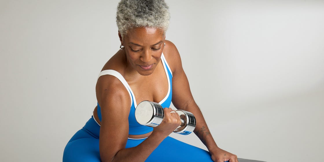 A woman in blue workout attire lifts a dumbbell while sitting on a bench.