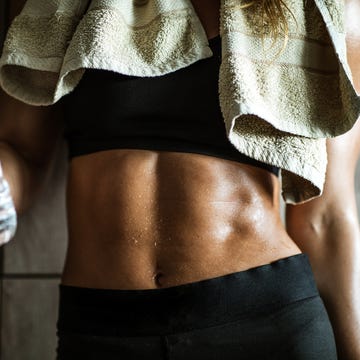 Unrecognizable athletic woman with abdominal muscles on water break in dressing room.