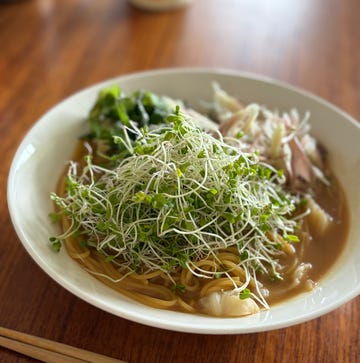 bowl of noodle soup with sprouts and vegetables on a wooden table with chopsticks.