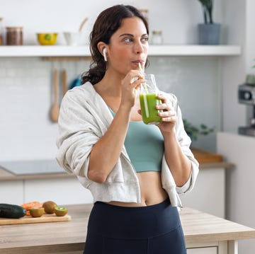 kind sporty woman drinking a healthy green smoothie standing in the kitchen at home.