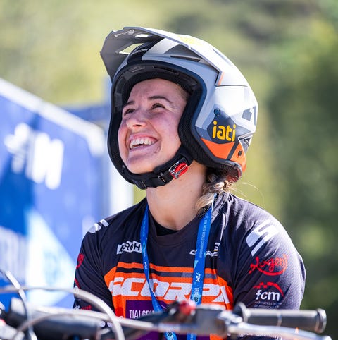 motocross rider smiling with helmet and orange gear.